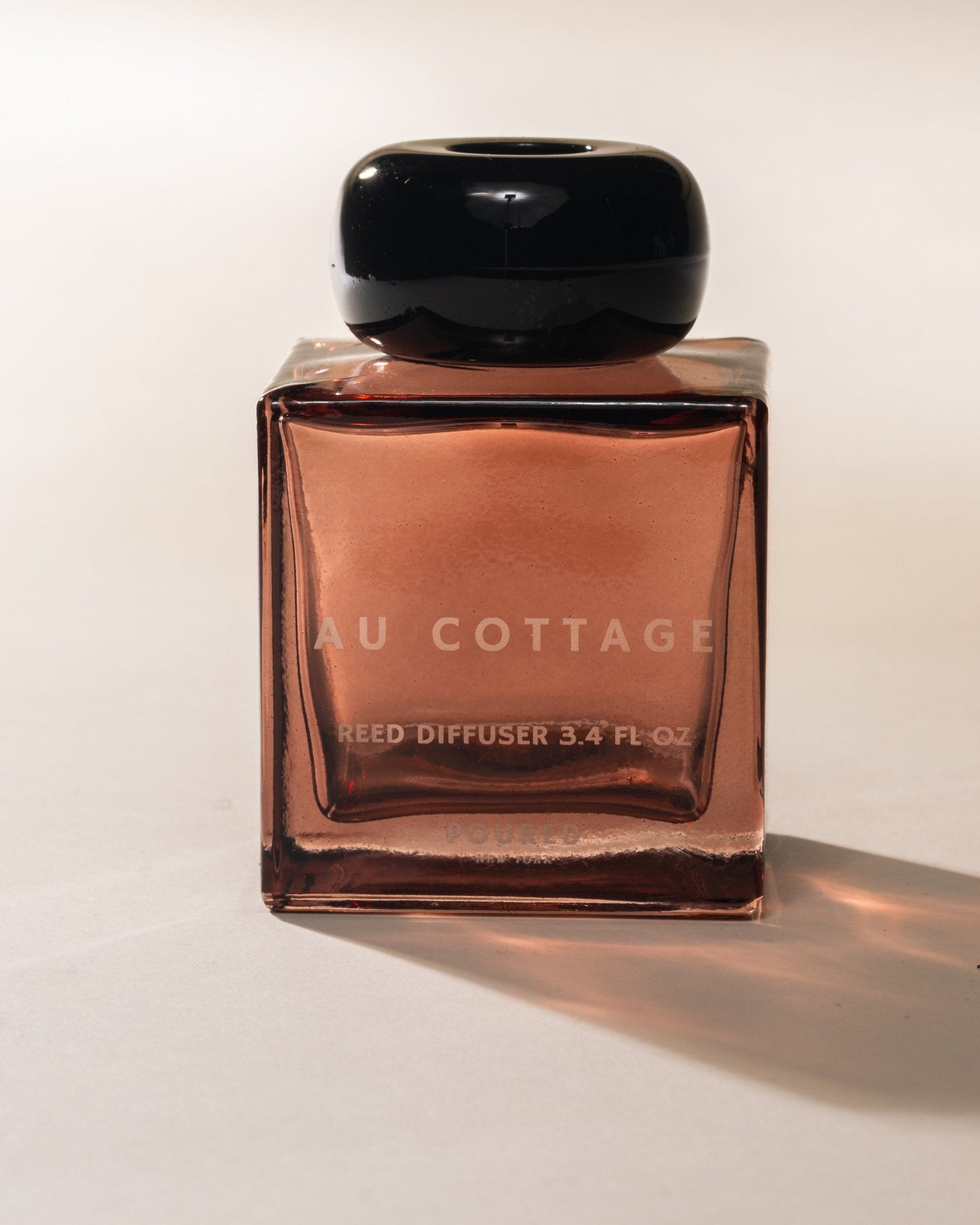 Au Cottage square shaped reed diffuser bottle with a black cap on a light background
