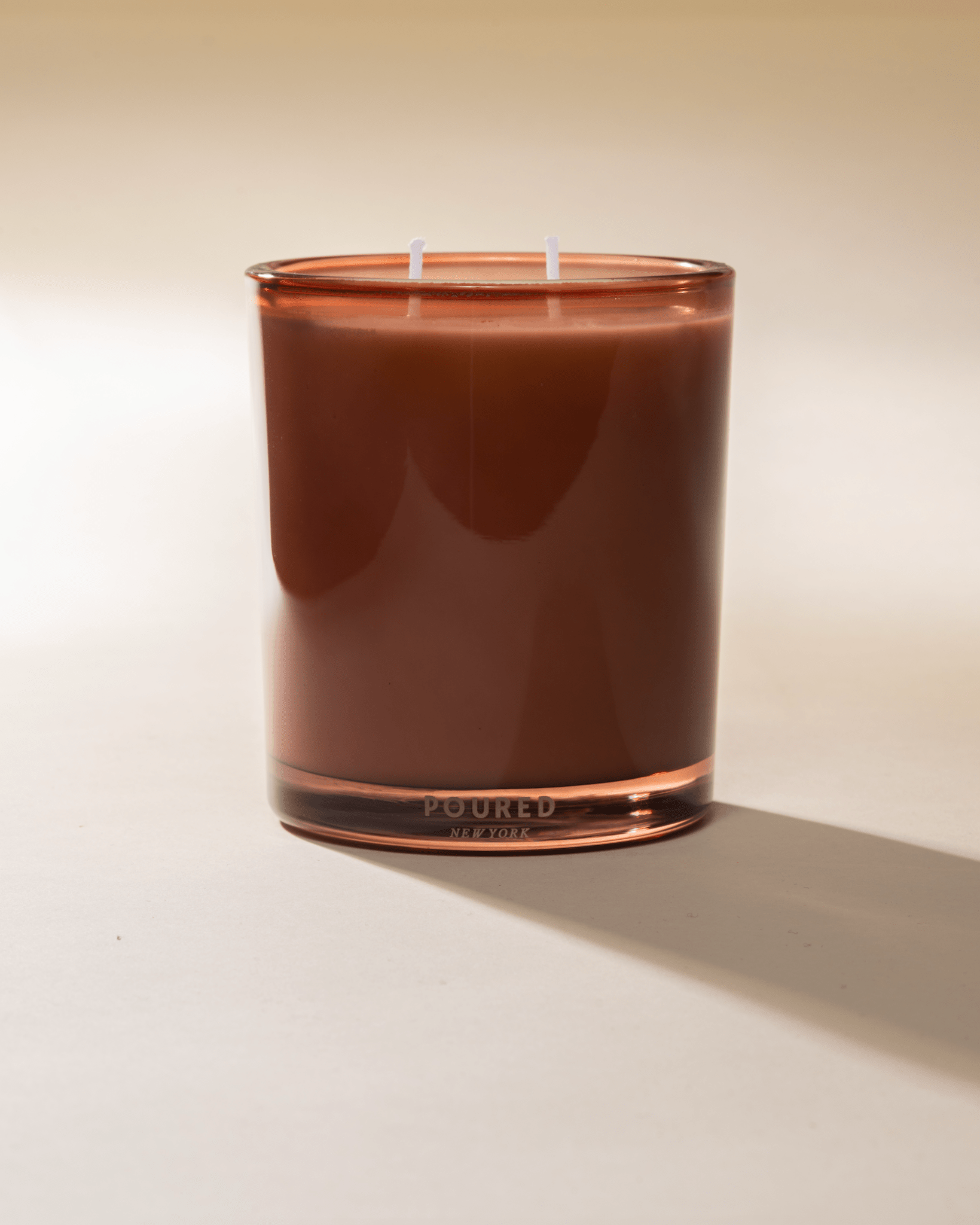 Poured New York 'Au Cottage' nude colored glass two wick candle on a neutral background