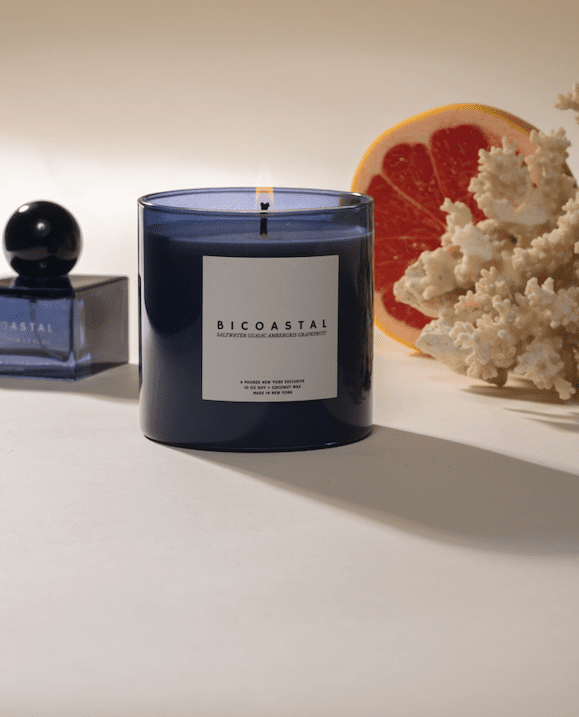 Poured New York 'Bicoastal' lifestyle shot with a blue candle and blue perfume on a beige background