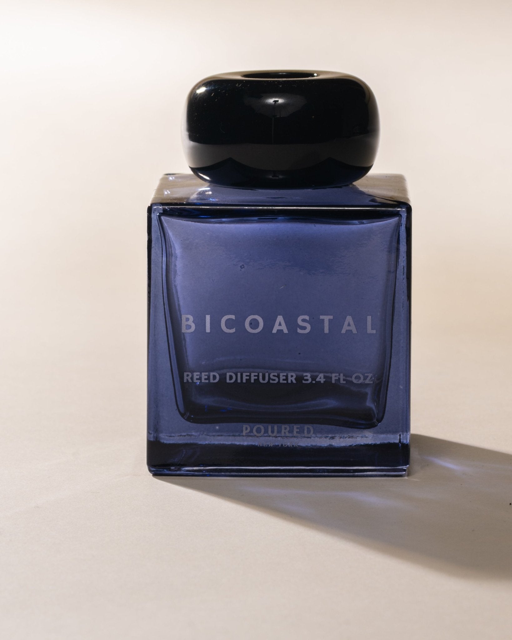 Poured New York 'Bicoastal' blue reed diffuser with black cap on a beige background