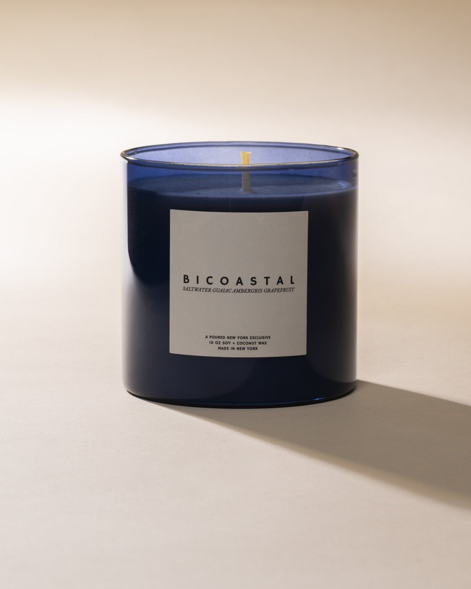 BICOASTAL candle in a dark glass container with a white label on a beige background