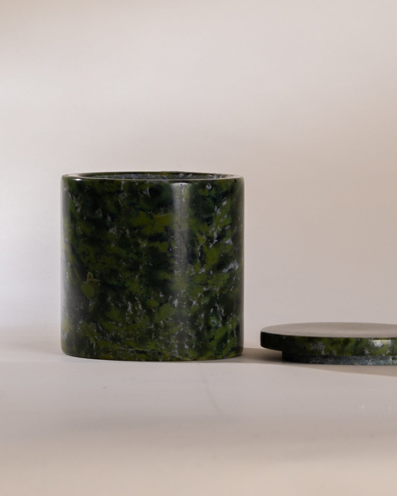 Moss green marble cylindrical container with matching lid sitting next to the vessel on a light beige background