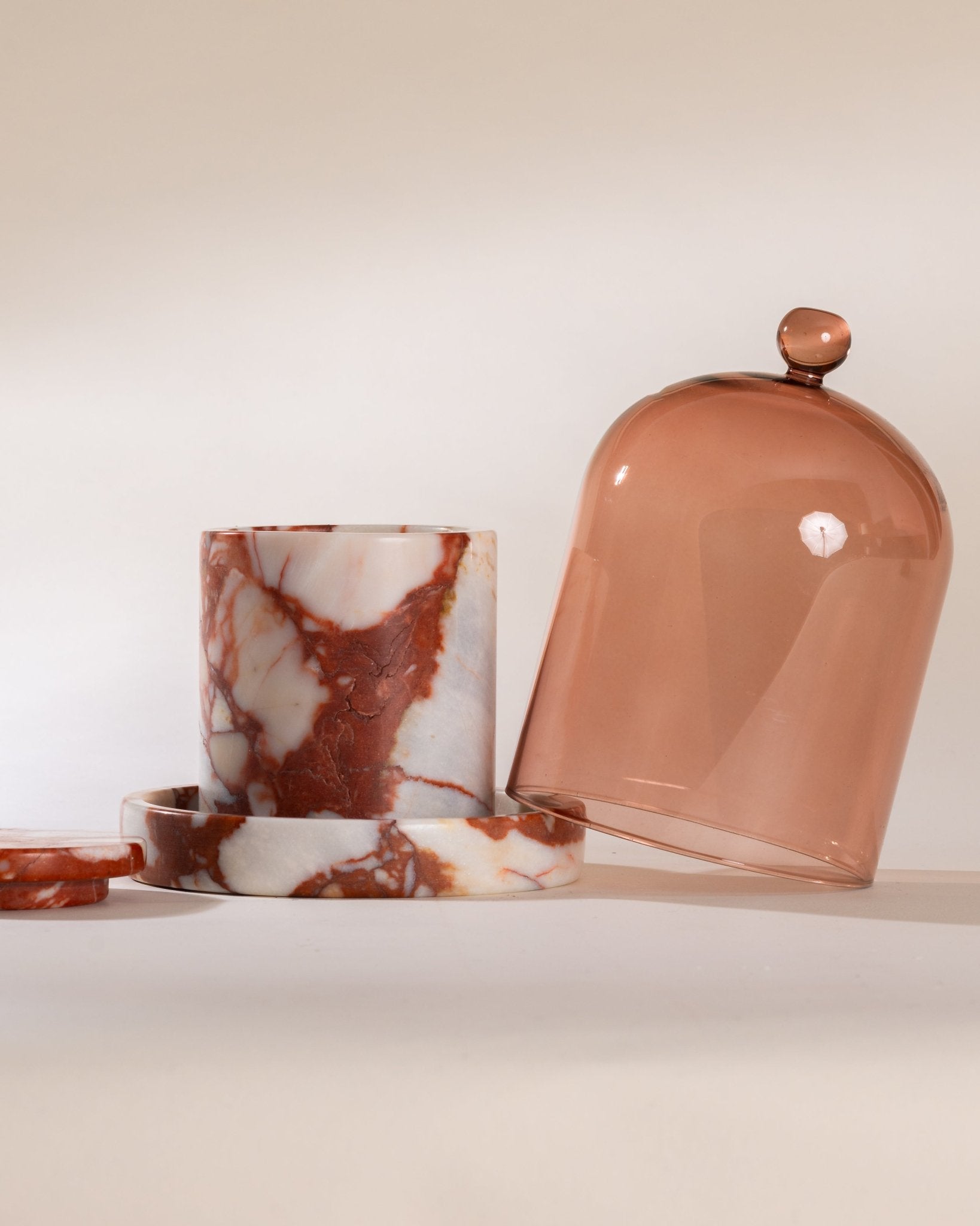 Cylindrical container with marbled pattern sitting on a matching red marble cloche base and a dome-shaped lid on a light background