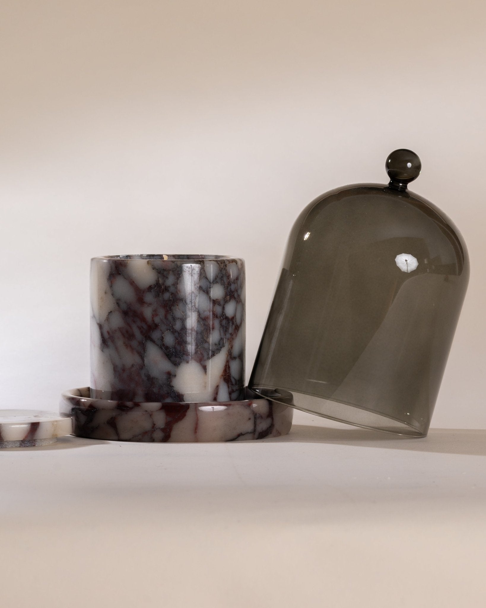 Marble-patterned candle siting on a matching purple marble cloche base and smoked glass dome on a neutral background