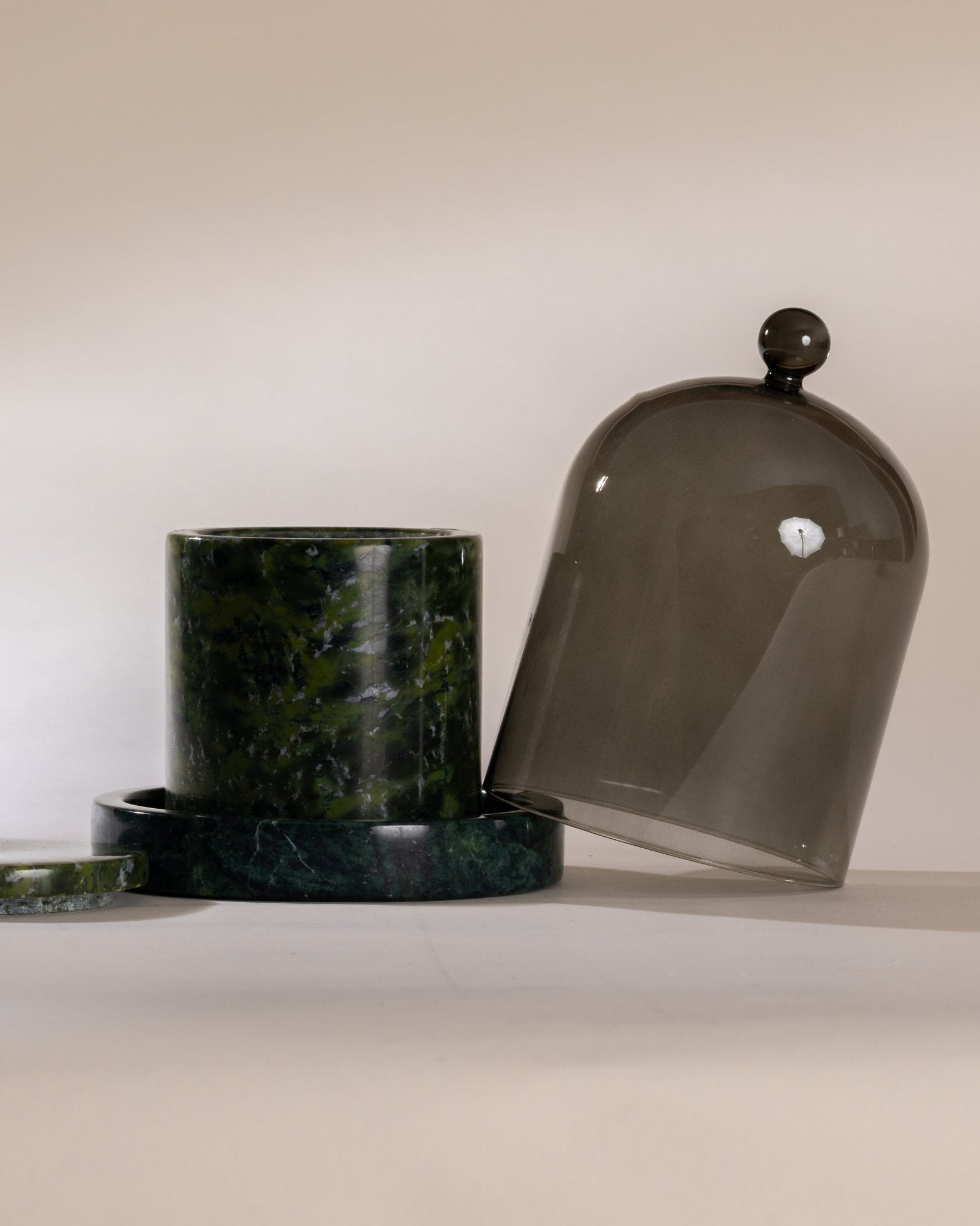 Two decorative containers, one moss marble vessel and one moss cloche base with moss colored glass on a neutral background.