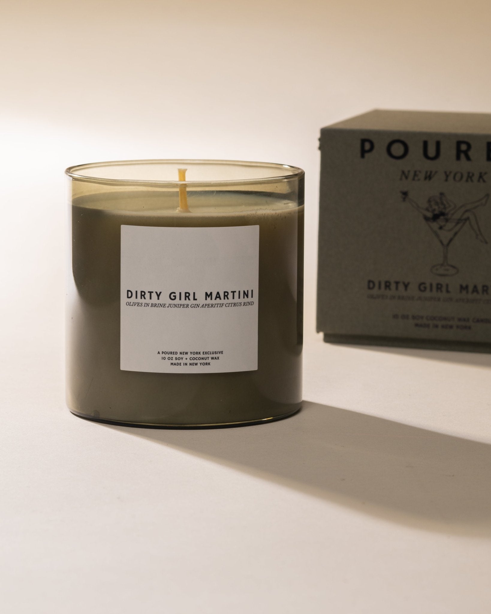 Poured New York 'Dirty Girl Martini' candle in olive green glass with a matching box with a girl in a martini decal on a neutral background