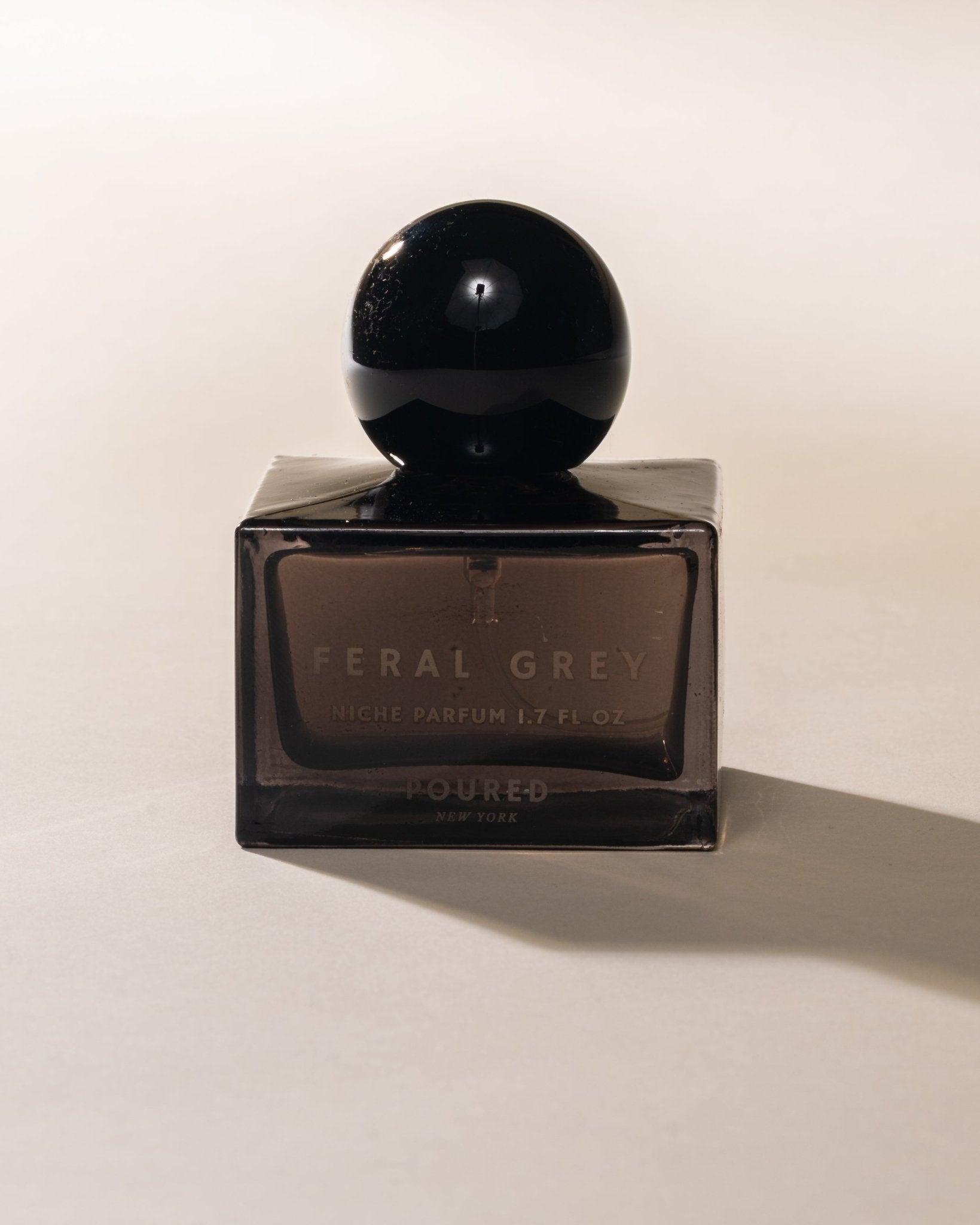 Poured New York 'Feral Grey' grey square niche parfum bottle with a black circular cap on a neutral background.