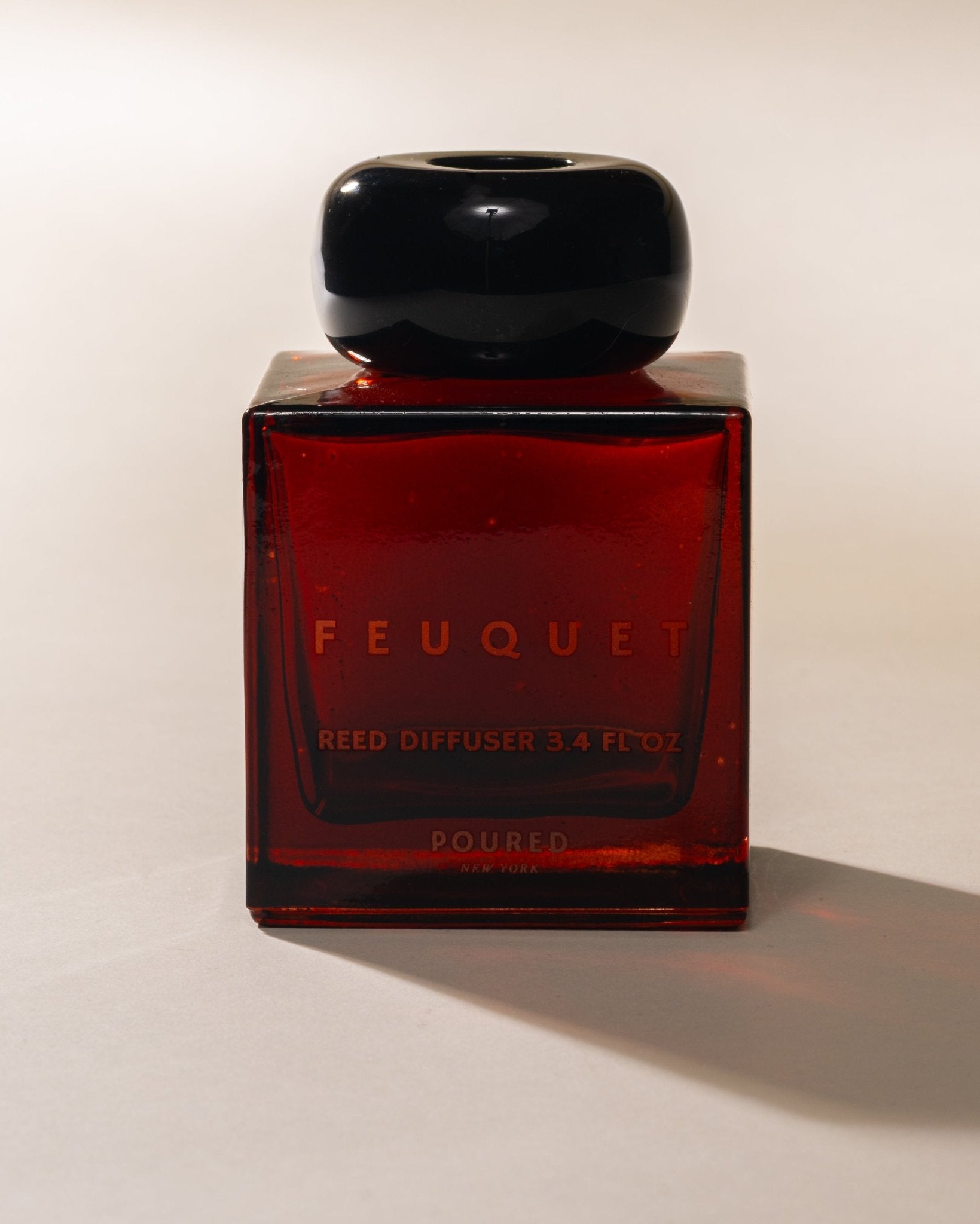 Red FEUQUET reed diffuser bottle with black cap on a white background