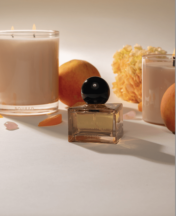 Poured New York Flesh & Fuzz Lifestyle shot with niche parfum in the foreground and the two candles in the background.