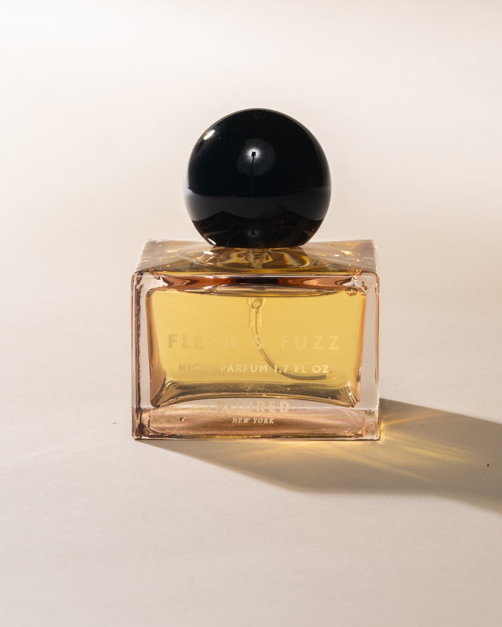 Poured New York Niche Parfum labeled 'Flesh & Fuzz' in a square peach glass and black circular cap on a neutral background