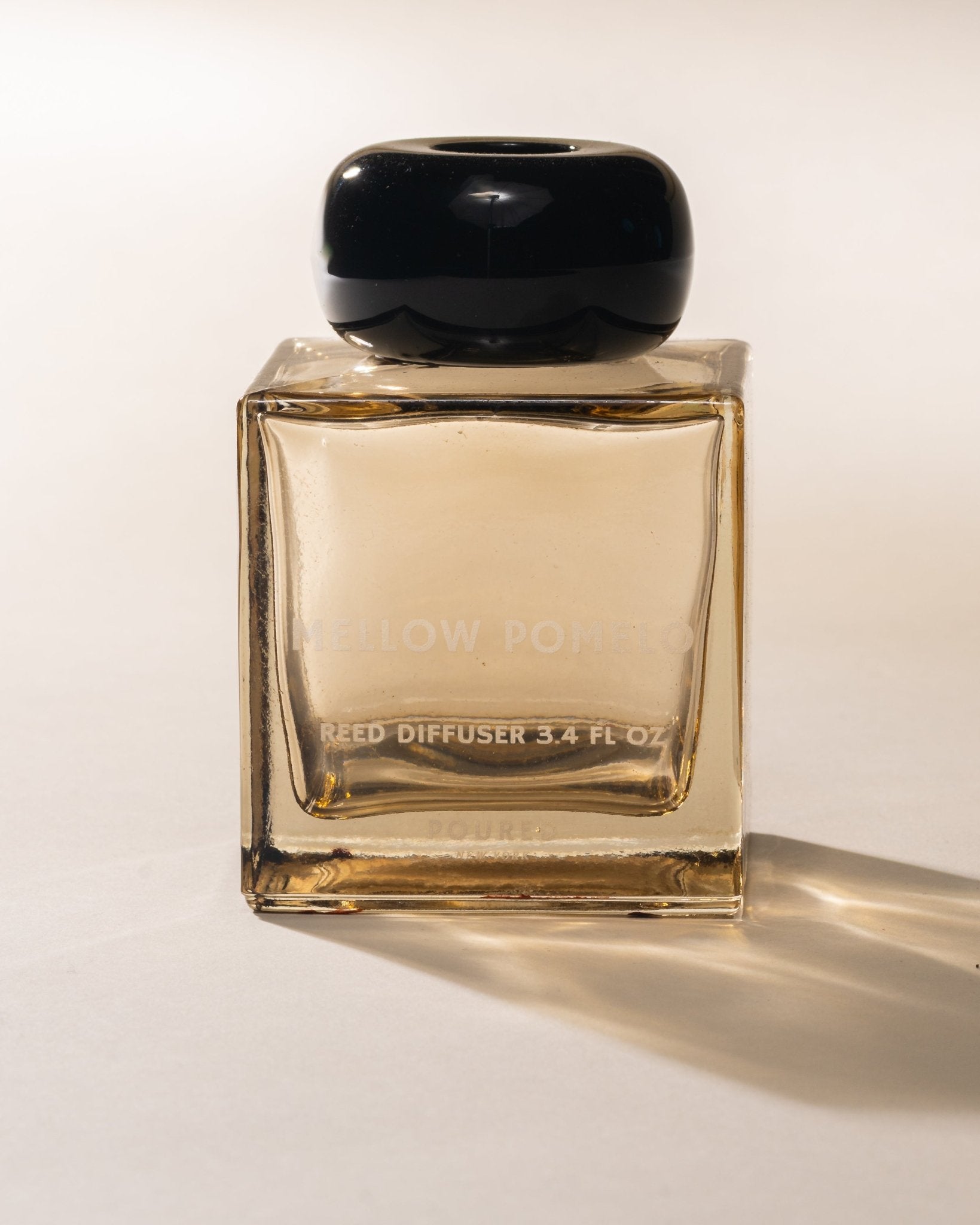 Poured New York 'Mellow Pomelo' Reed Diffuser square glass with circular black cap on neutral background.