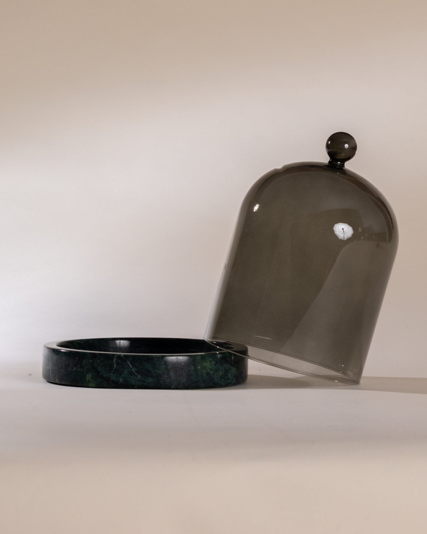 Moss green marble cloche base with a matching moss marble glass dome cover on a beige background