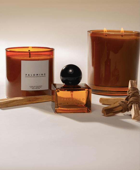 Poured New York 'Palomino' fragrances with a niche parfum glass square bottle in the foreground and the two candles in the background with palo santo and leather decor on a neutral background