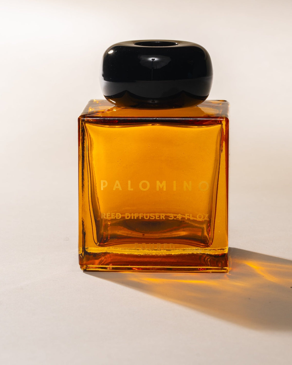 Amber glass 'Palomino' reed diffuser bottle with black cap on a white background
