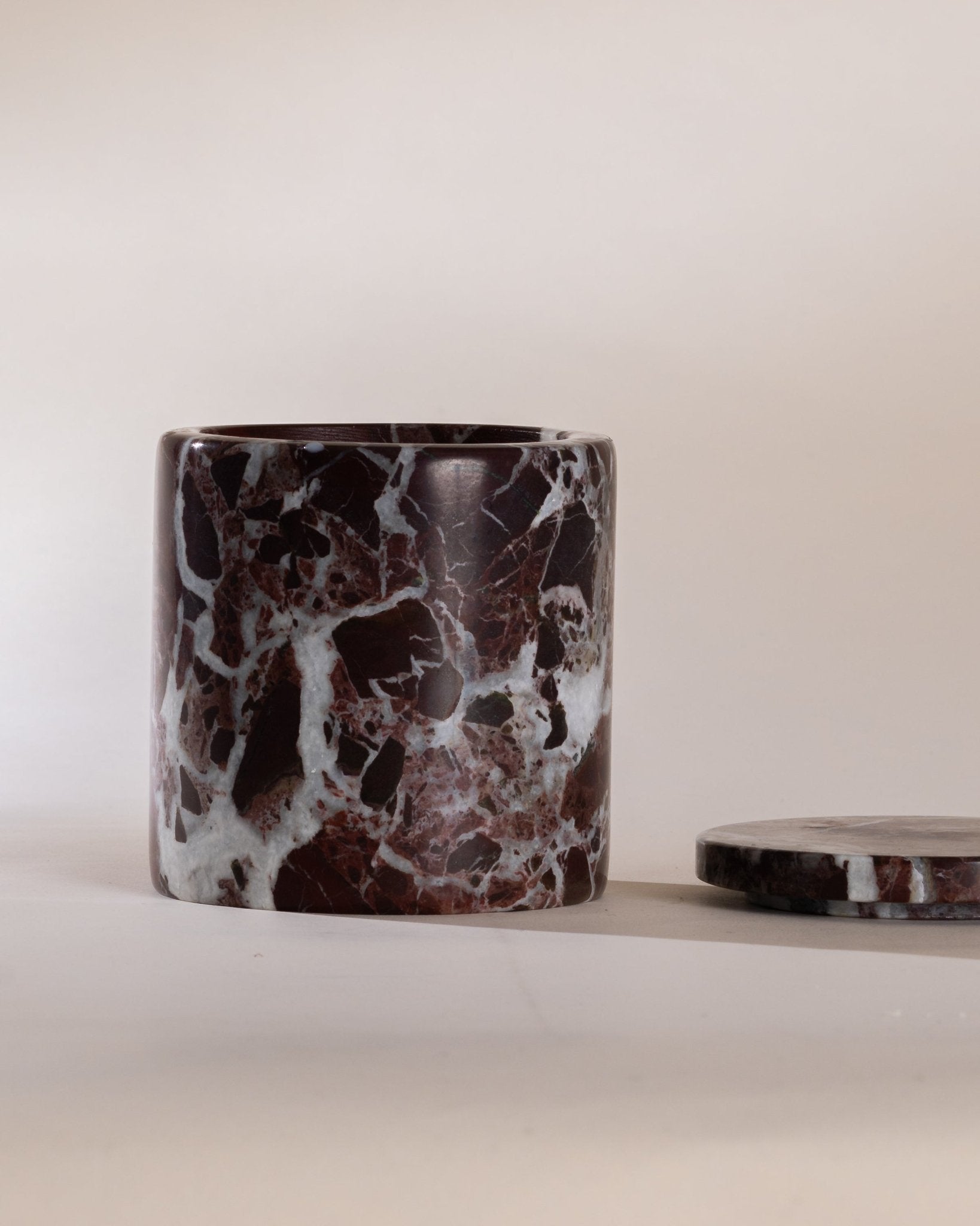 Dark red marble-patterned candle holder with a matching marble lid next to the vessel on a neutral background