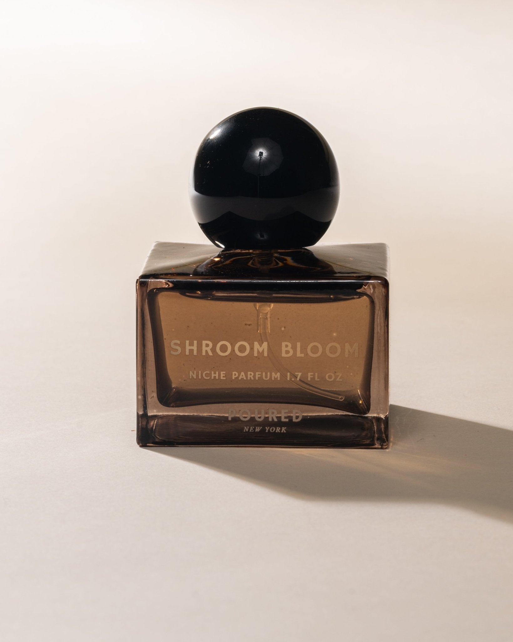 Perfume bottle labeled 'Shroom Bloom' on a light background