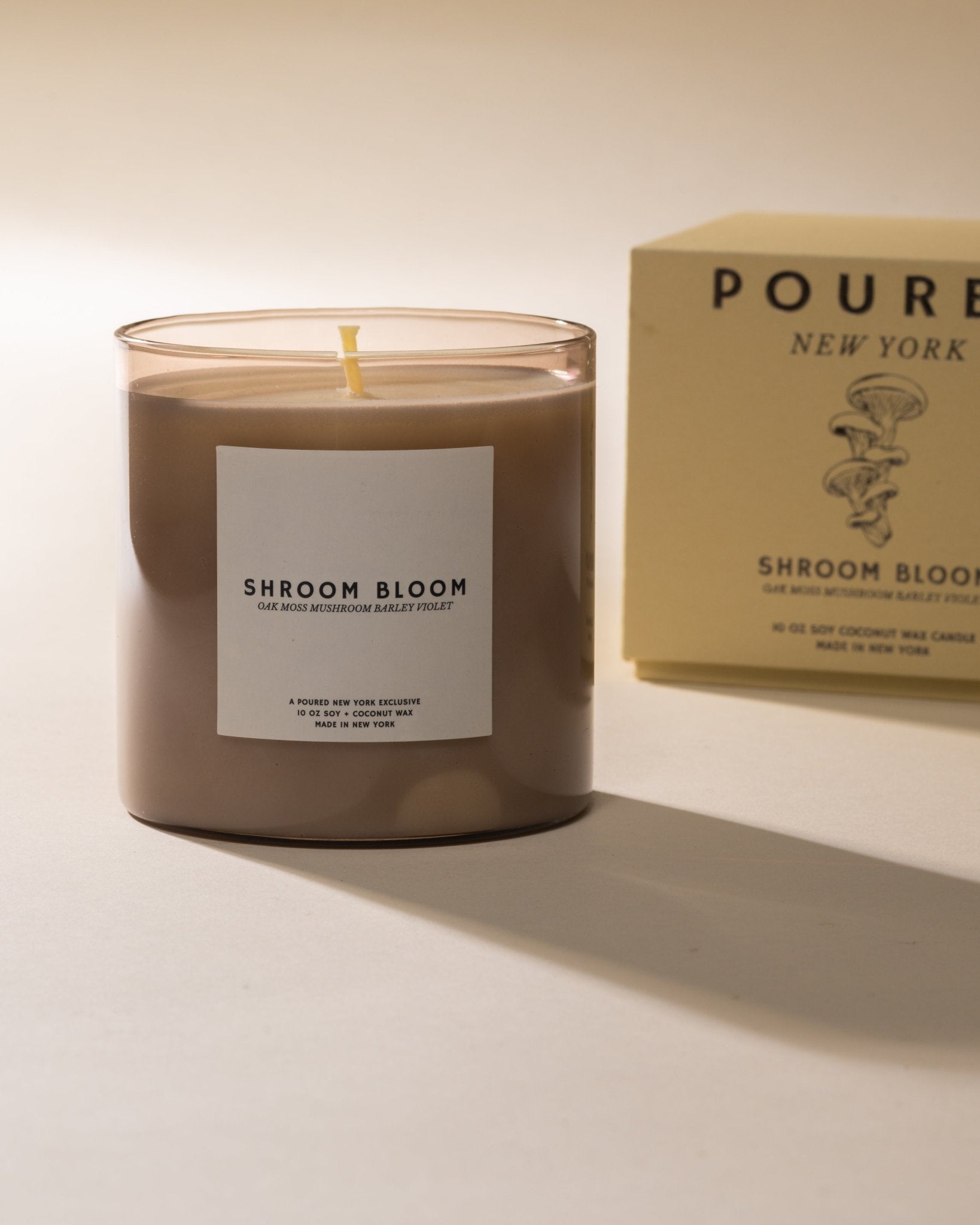 Candle labeled 'Shroom Bloom' with a box in the background on a light beige background