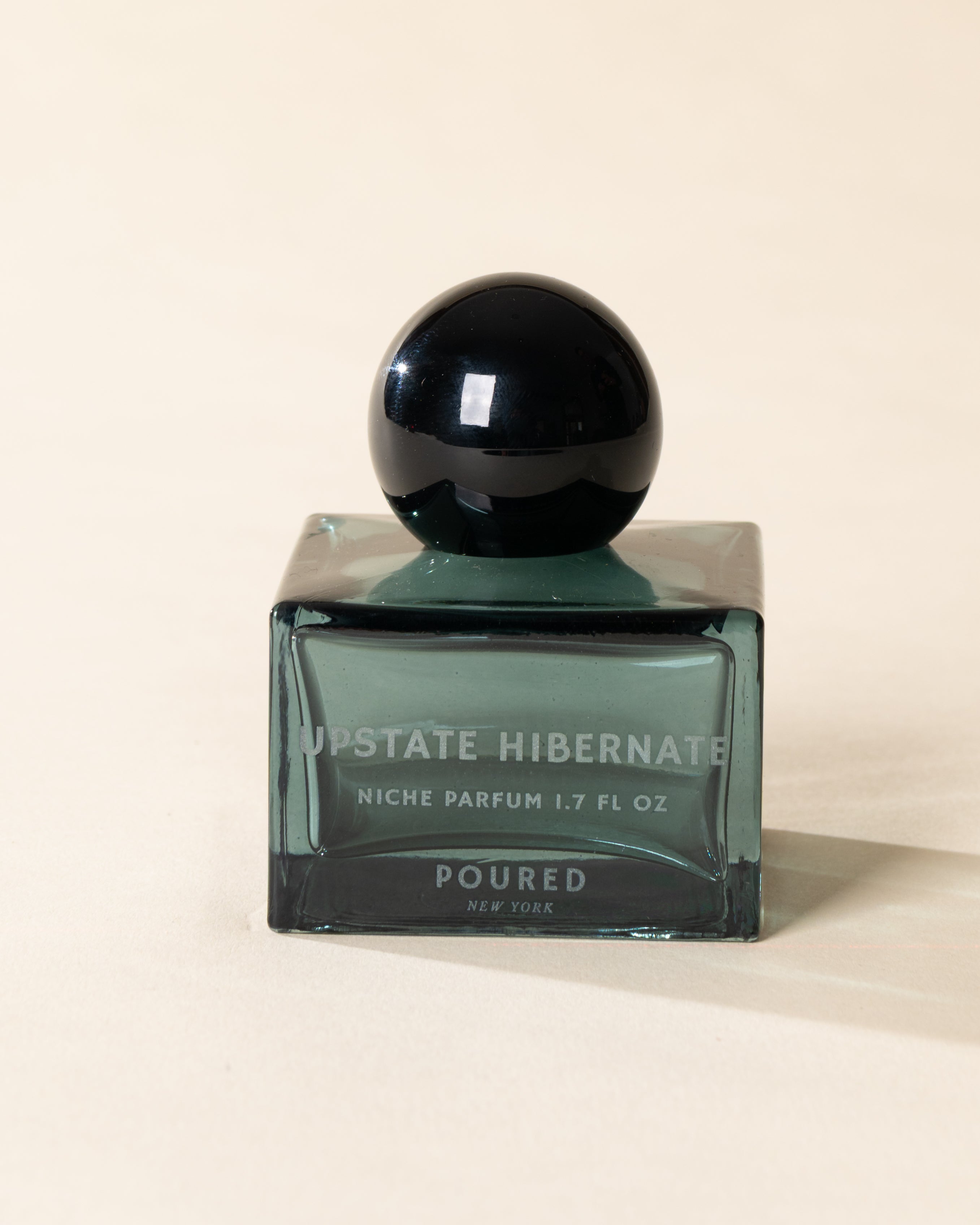 Poured New York 'Upstate Hibernate' niche parfum in a teal glass bottle on a neutral background