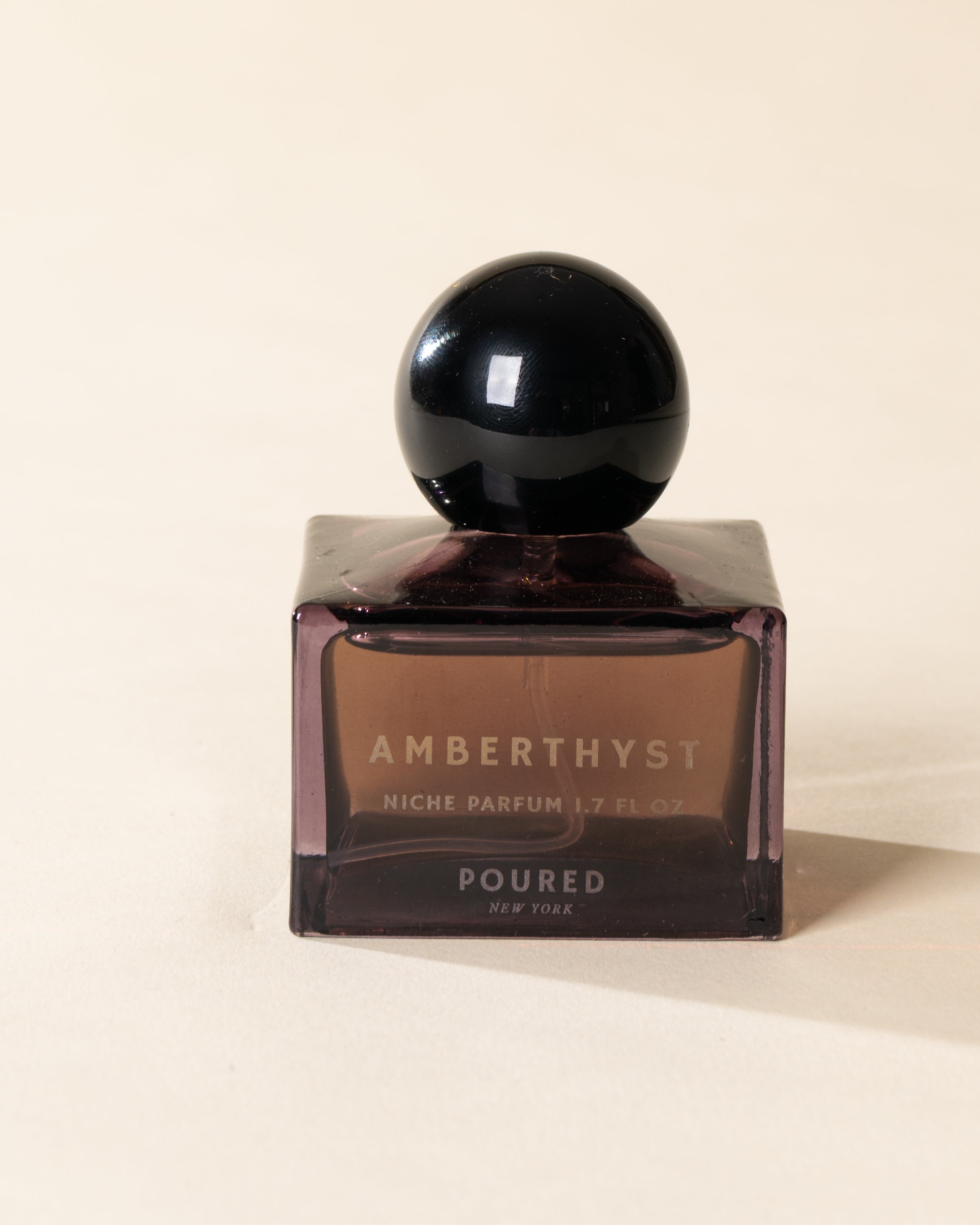 Poured New York 'Amberthyst' niche parfum in a purple glass bottle on a neutral background
