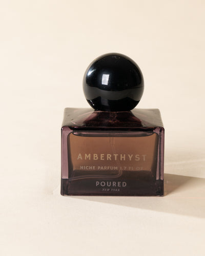 Poured New York 'Amberthyst' niche parfum in a purple glass bottle on a neutral background