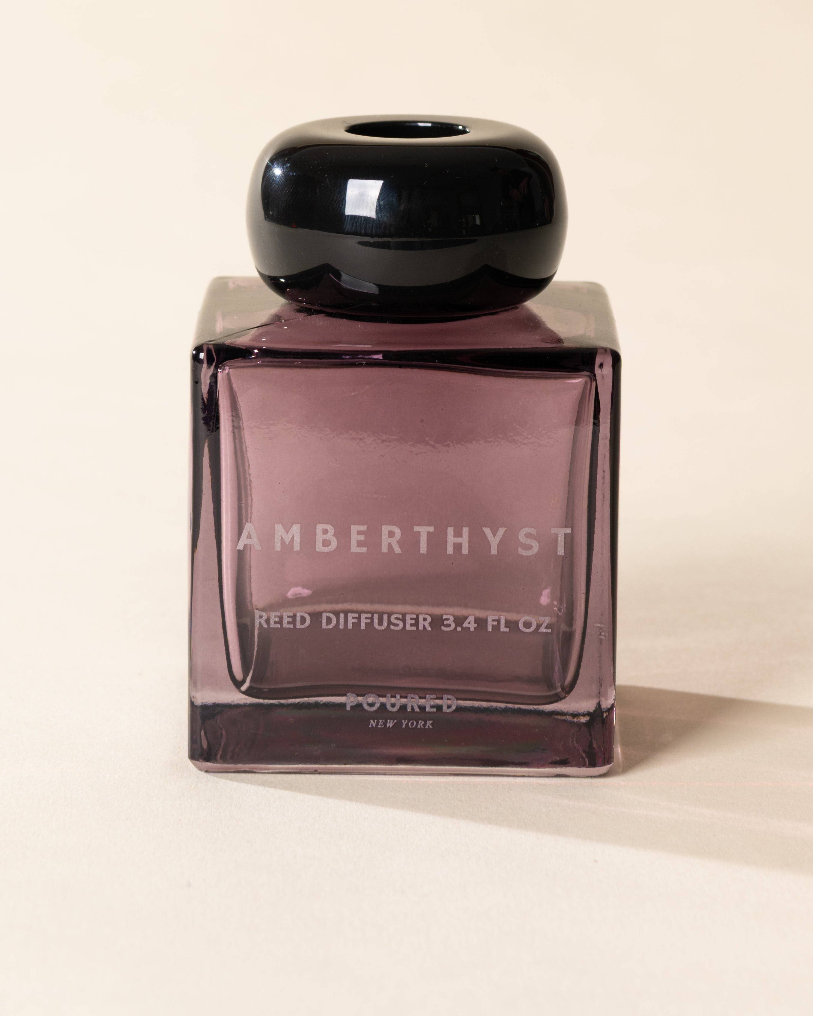 Poured New York 'Amberthyst' reed diffuser in a purple glass vessel on a neutral background