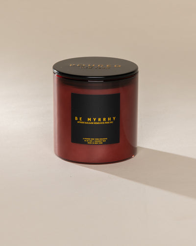 Poured New York 'Be Myrrhy' 10 oz red glass coconut soy wax candle on a neutral background