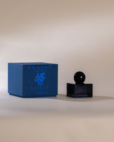Poured New York 'Bicoastal' blue perfume bottle with black cap on a beige background