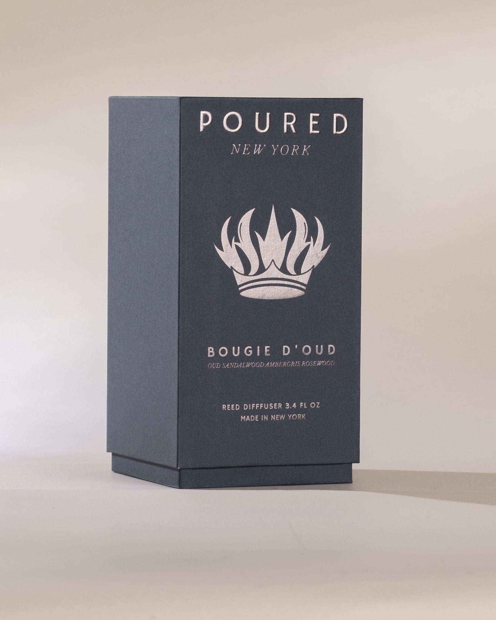 Dark blue reed diffuser box with 'POURED NEW YORK' branding and a crown decal on a beige background