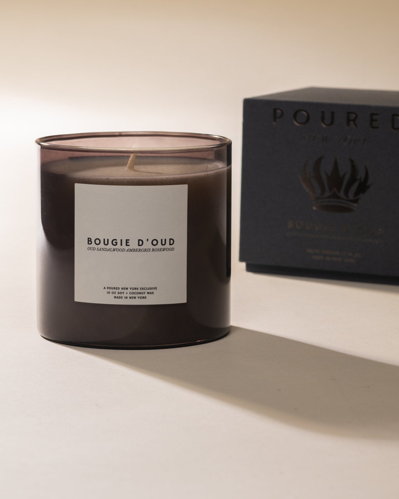 Candle labeled 'Bougie D'Oud' next to a black box with 'POURED' branding and a crown decal on a light background