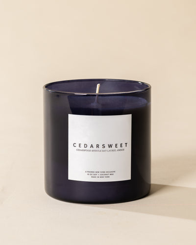 Poured New York 'Cedarsweet' 10 oz navy glass soy wax candle on a neutral background