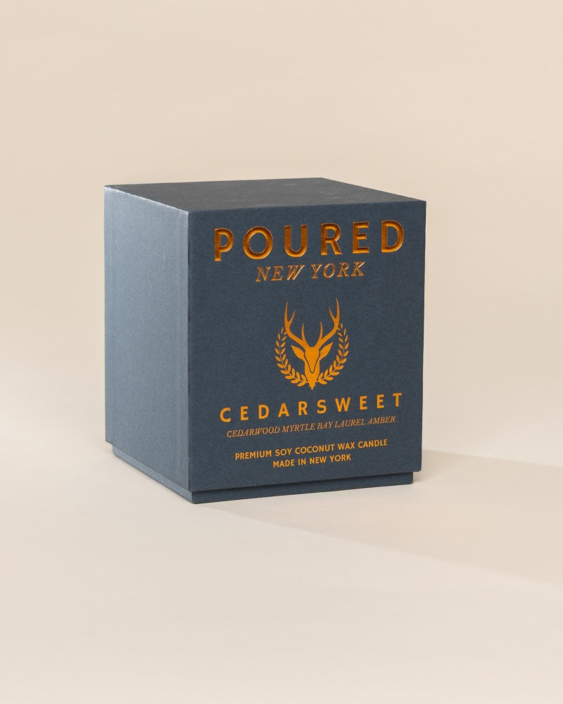 Poured New York 'Cedarsweet' candle box packaging on a neutral background