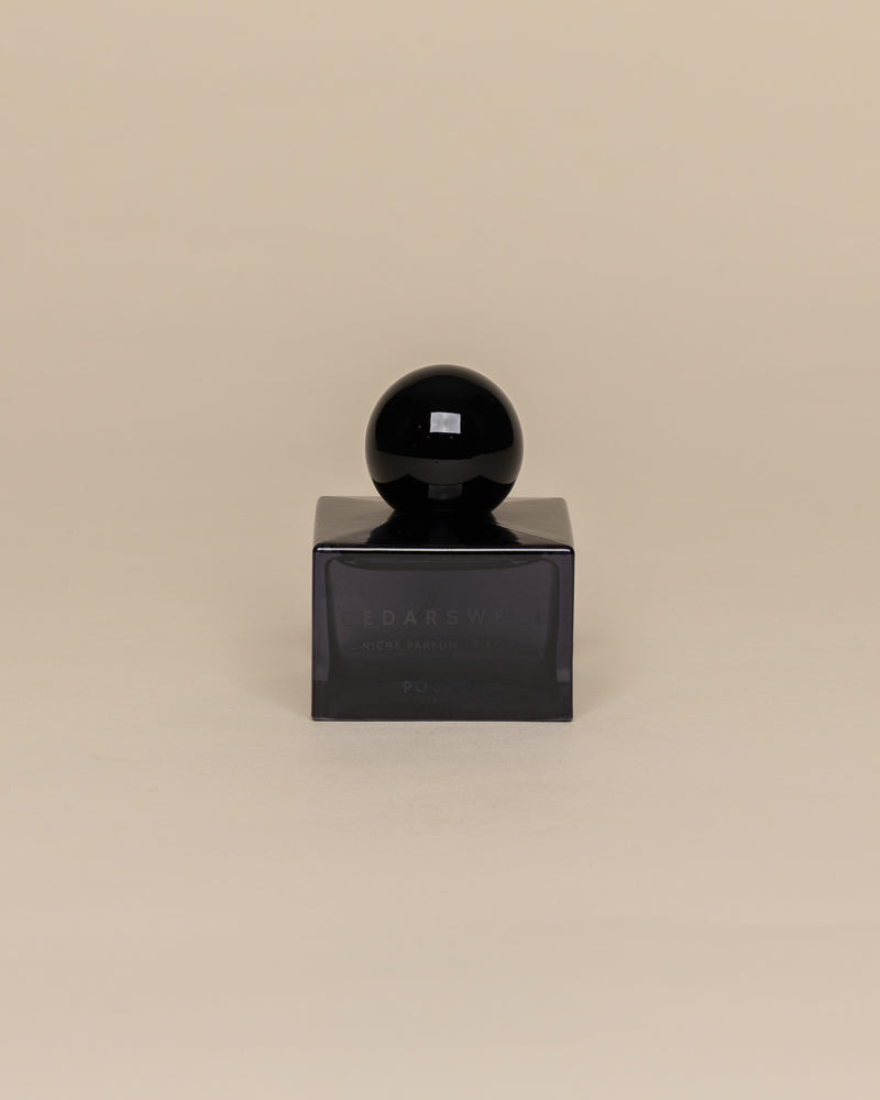 Poured New York 'Cedarsweet' niche parfum in a navy glass bottle on a neutral background