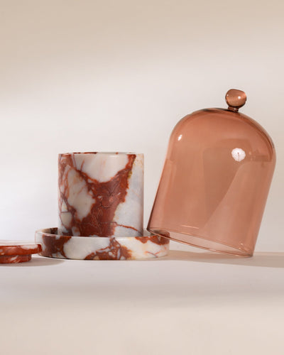 Cylindrical container with marbled pattern sitting on a matching red marble cloche base and a dome-shaped lid on a light background