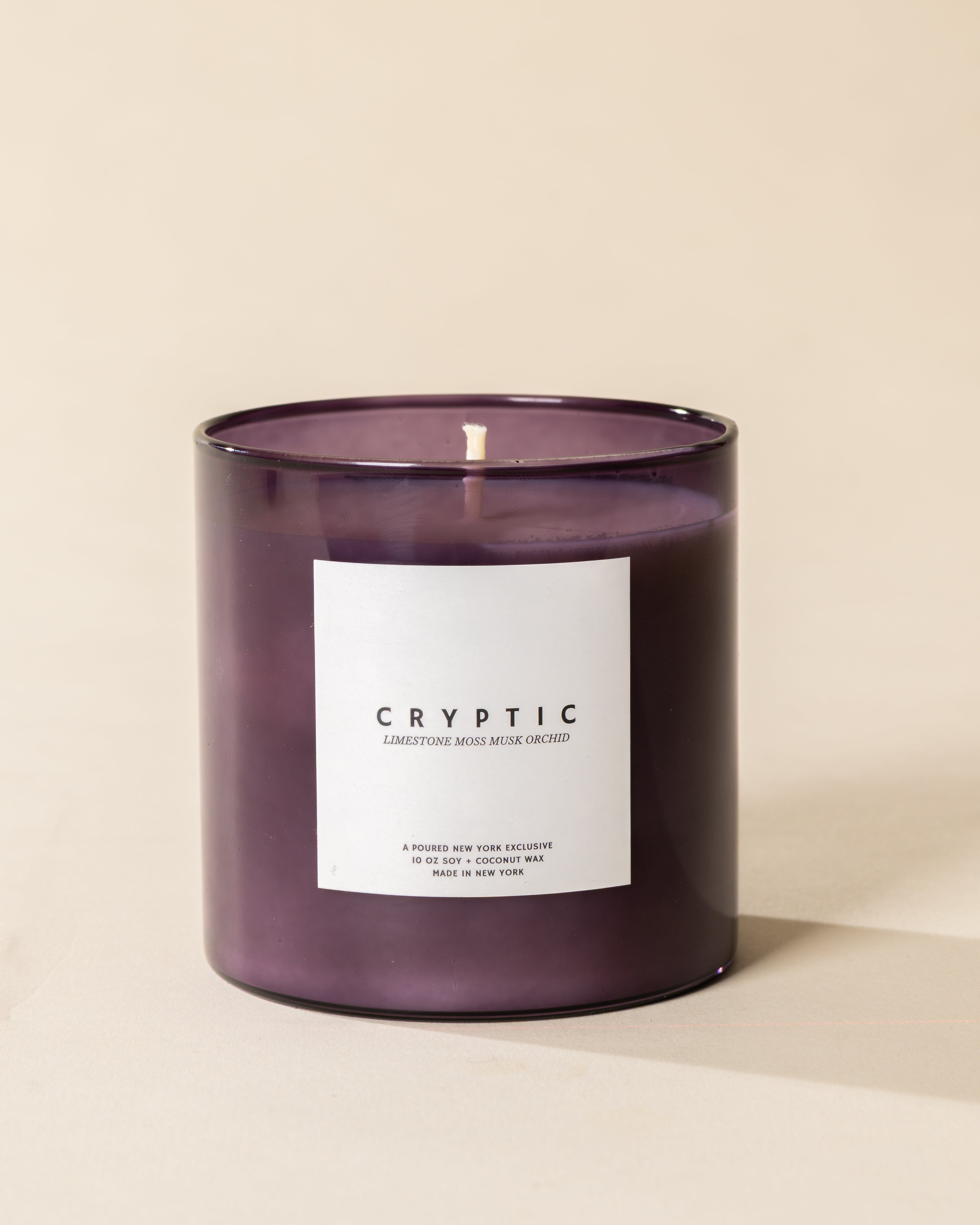 Poured New York 'Cryptic' 10 oz purple glass soy coconut wax candle on a neutral background