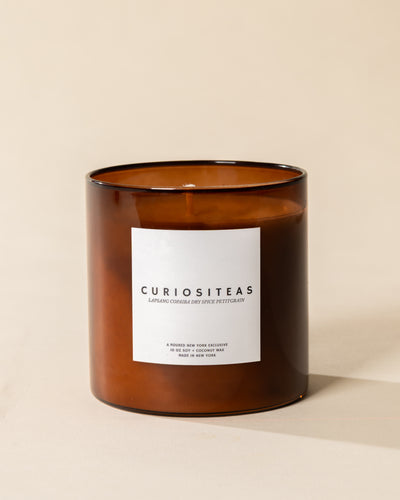 Poured New York 'Curiositeas' 10 oz brown glass soy wax candle on a neutral background