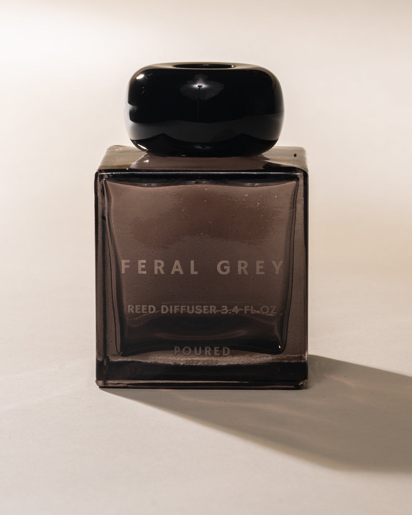 Poured New York 'Feral Grey' grey square reed diffuser with a black cap on a neutral background.