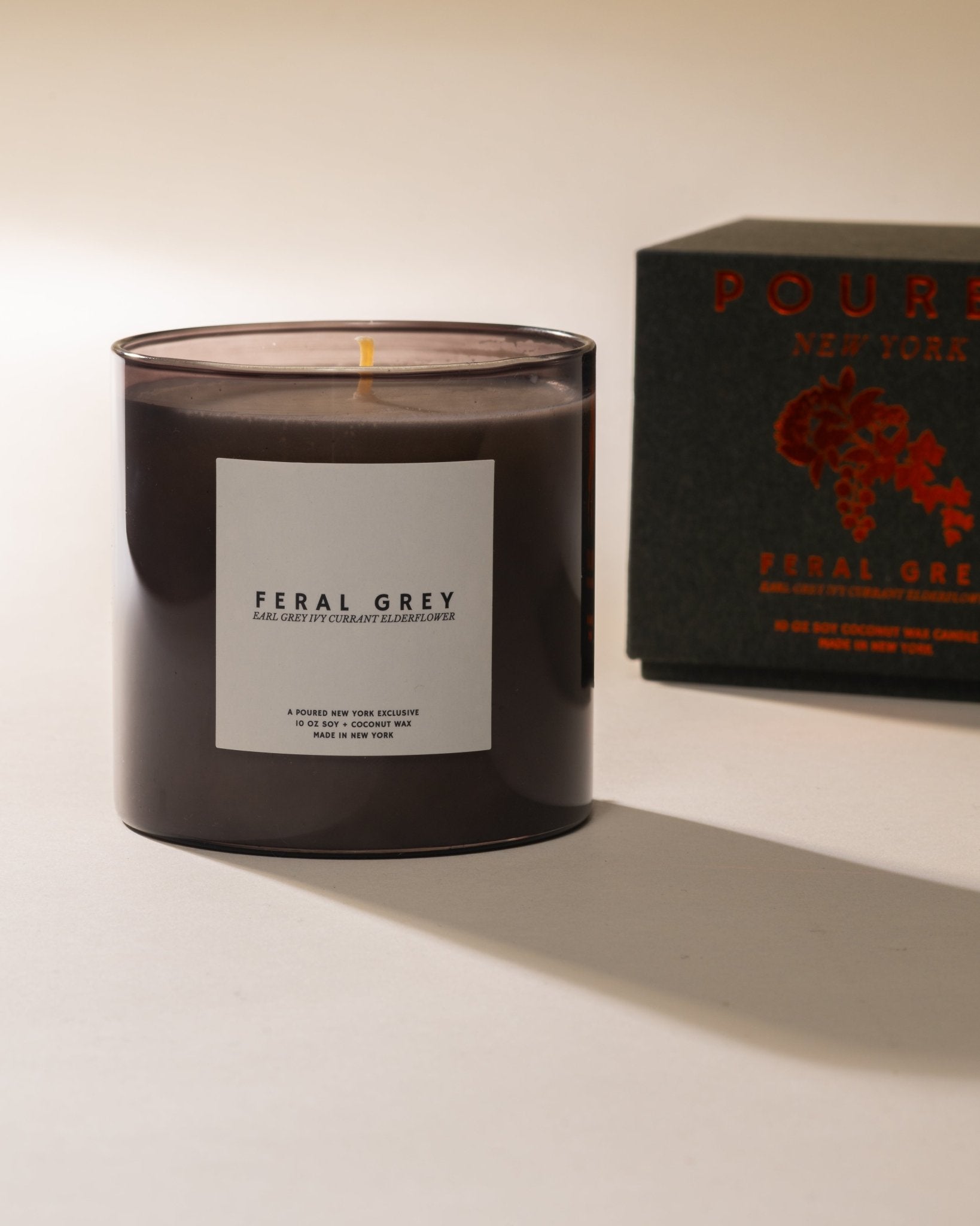Poured New York 'Feral Grey' candle in grey glass and a matching grey box with an ivy and currant decal on a neutral background.
