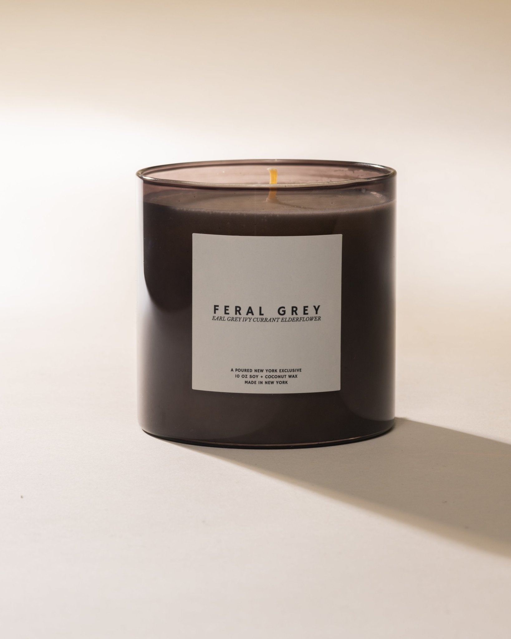 Poured New York 'Feral Grey' candle in grey glass on a neutral background.