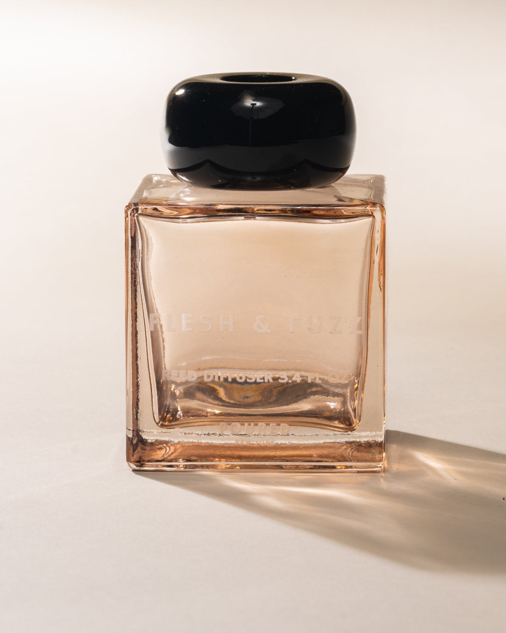 Poured New York reed diffuser labeled 'Flesh & Fuzz' in a peach square glass and black cap on a neutral background
