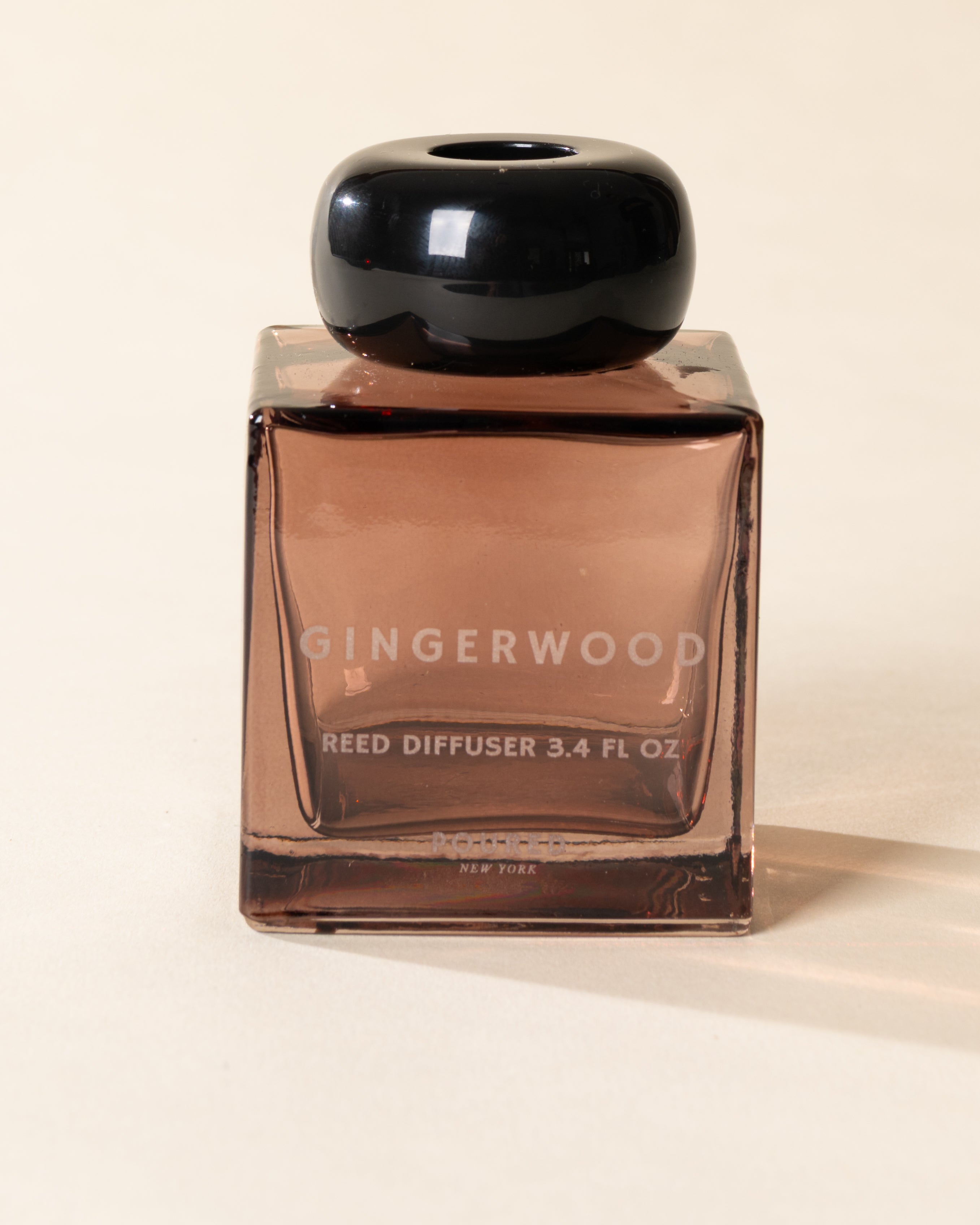 Poured New York 'Gingerwood' reed diffuser in a brown glass vessel on a neutral background