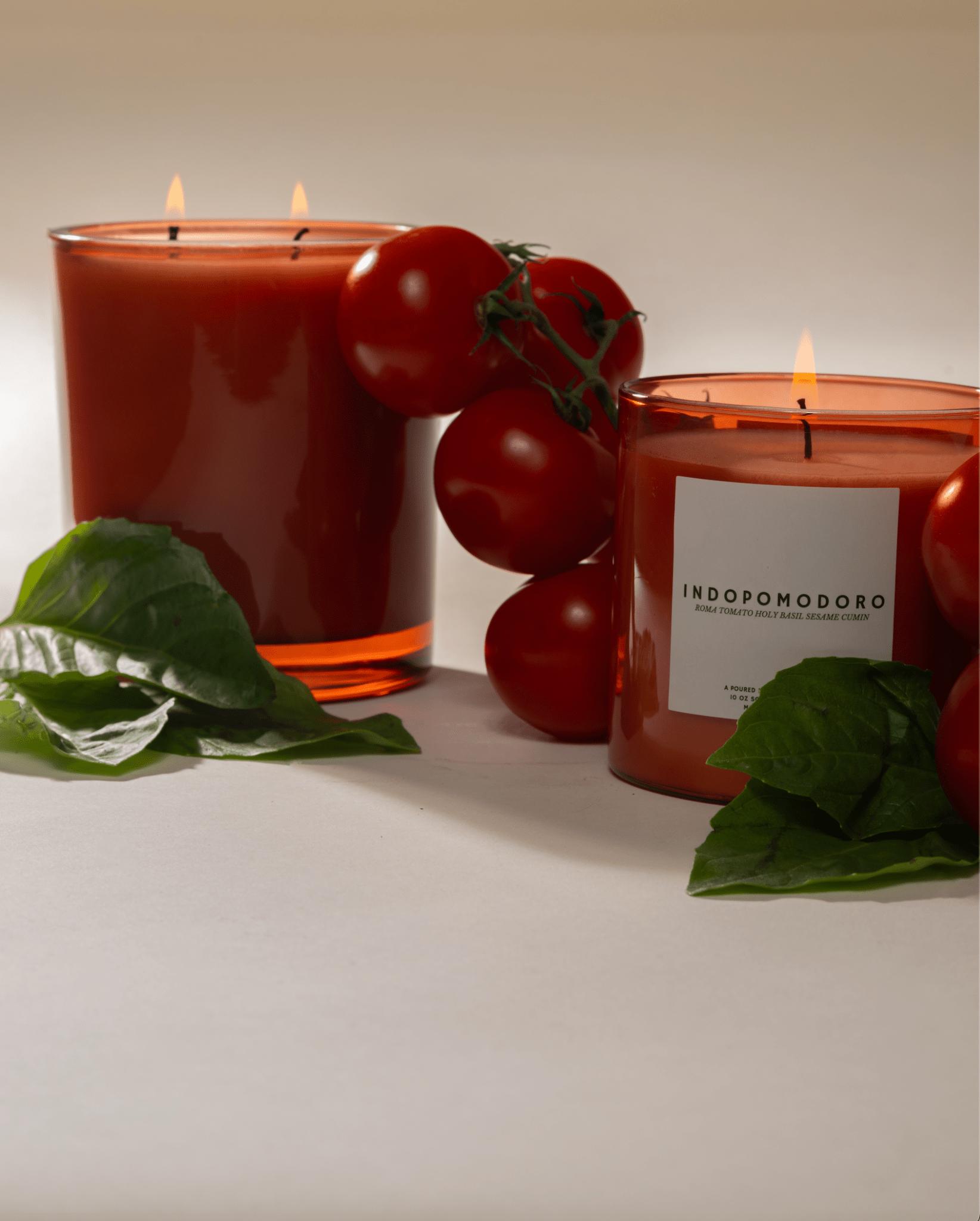 Two Poured New York 'Indopomodoro' candles with fresh Roma tomatoes and basil decor on a neutral background