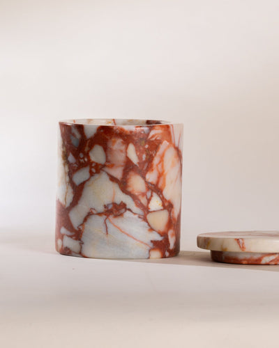 Red brick marble-patterned candle jar  with a matching marble lid to the side of the vessel on a light background
