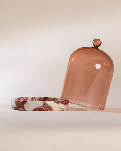 Decorative container with a red marble base and brick red tinted glass dome on a neutral background