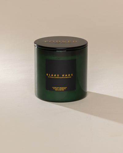 Poured New York 'Klaus Haus' 10 oz green glass coconut soy wax candle on a neutral background