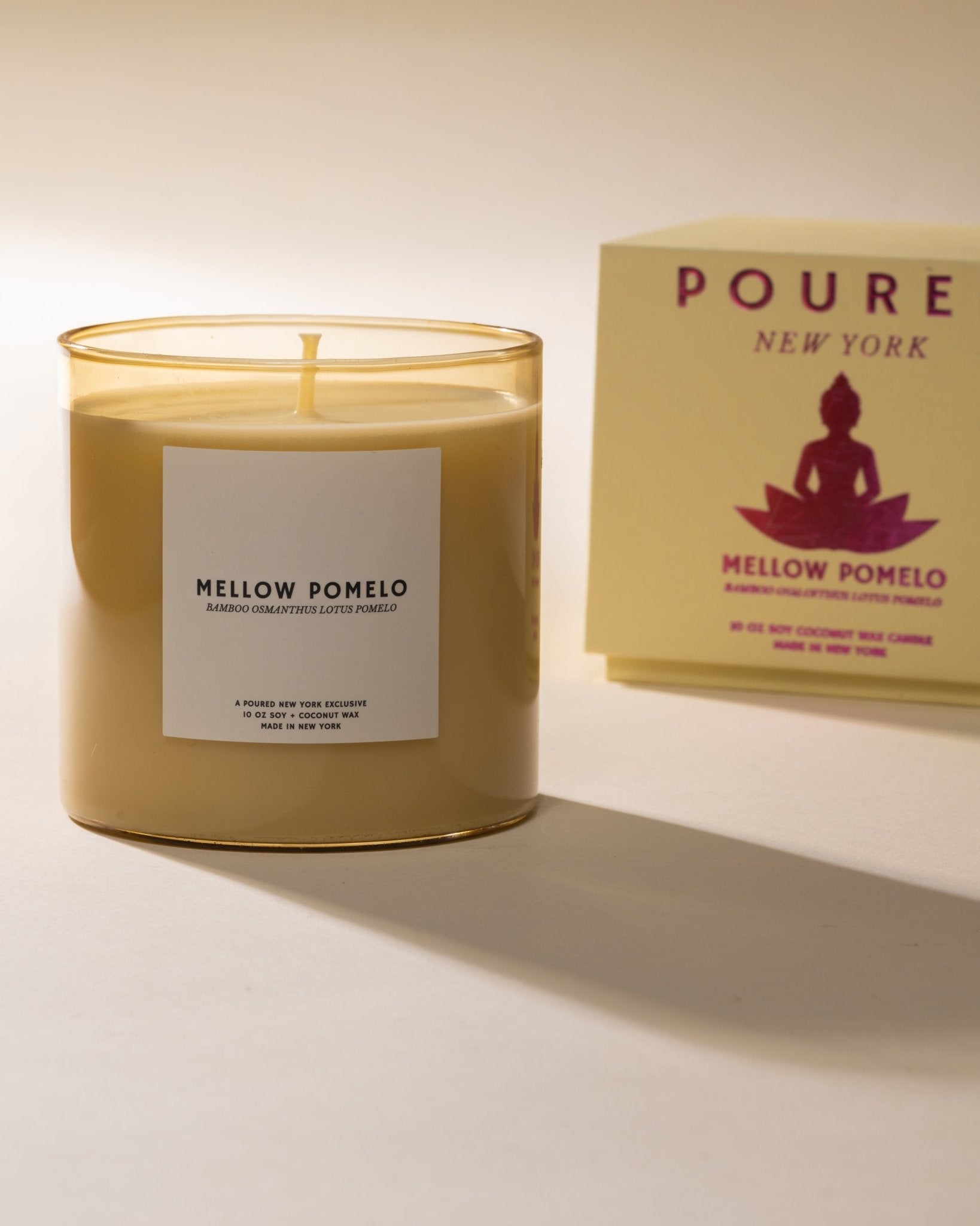 Candle labeled 'Mellow Pomelo' with packaging in the background on a neutral background