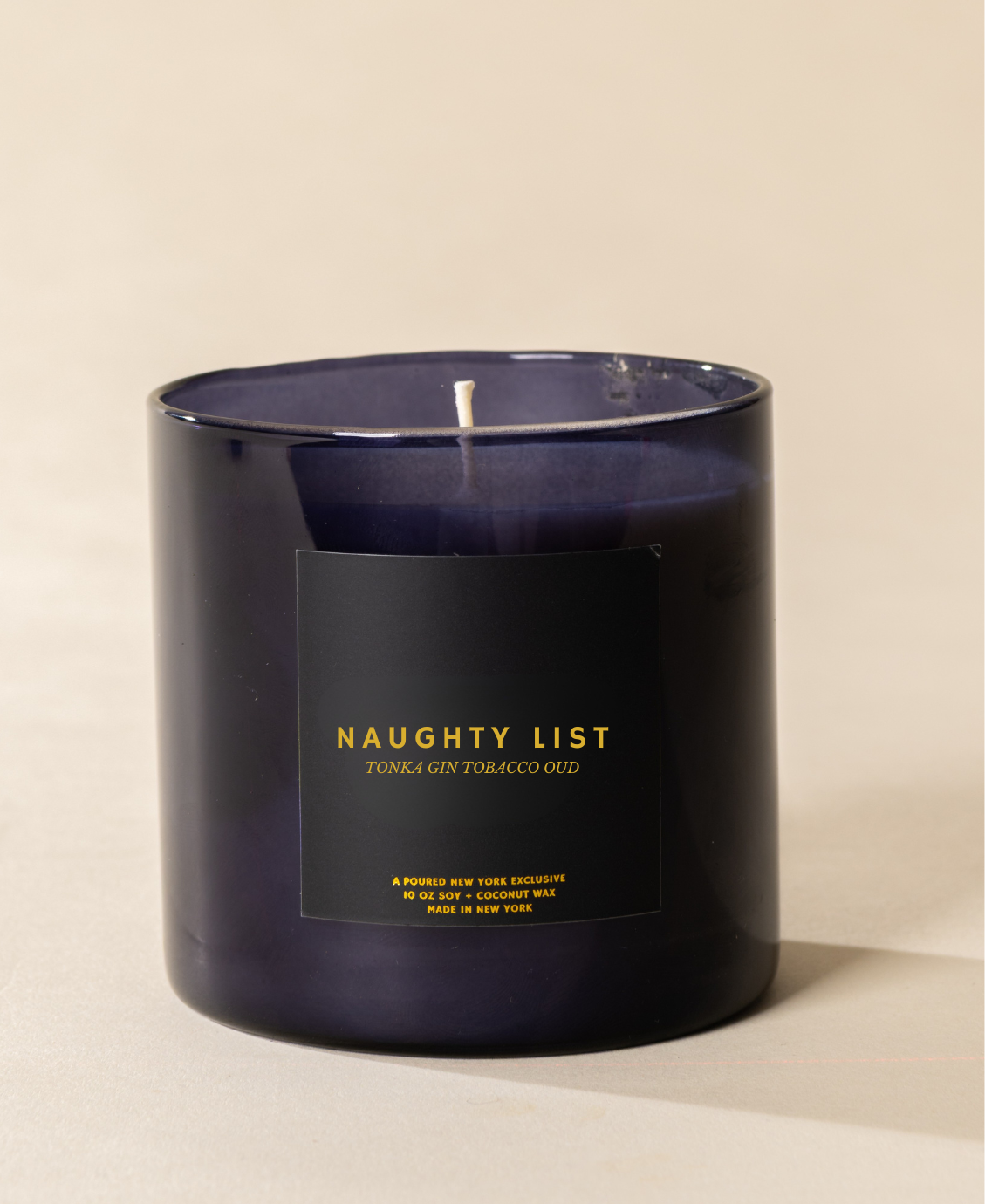 Poured New York 'Naughty List' 10 oz navy glass soy wax candle on a neutral background