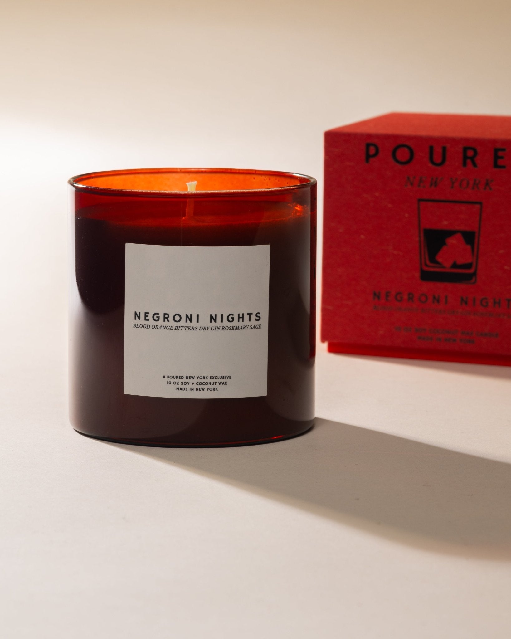 Poured New York 'Negroni Nights' candle in red glass jar with matching red candle box with a negroni glass decal on a neutral background.