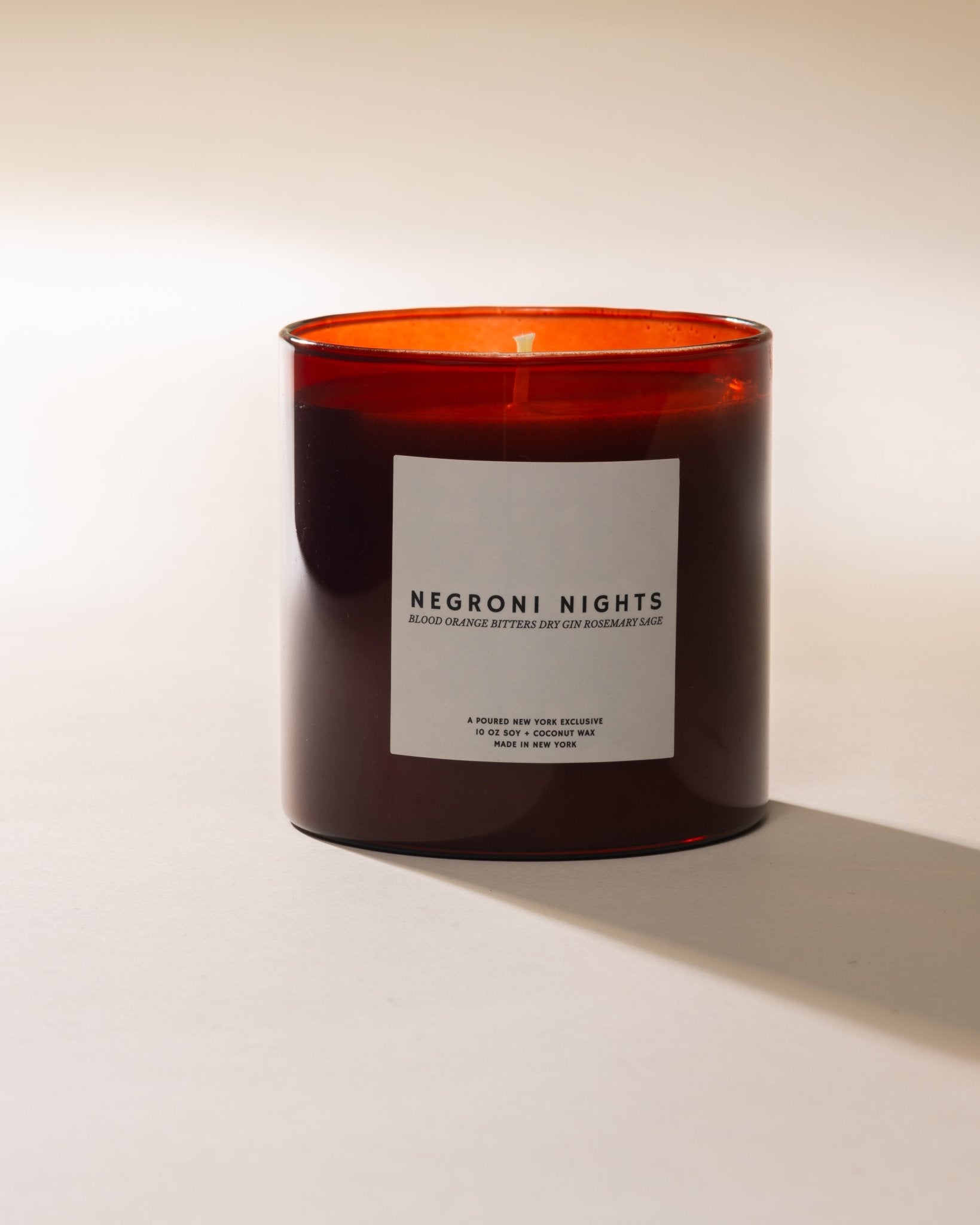 Poured New York 'Negroni Nights' candle in red glass jar on a neutral background.
