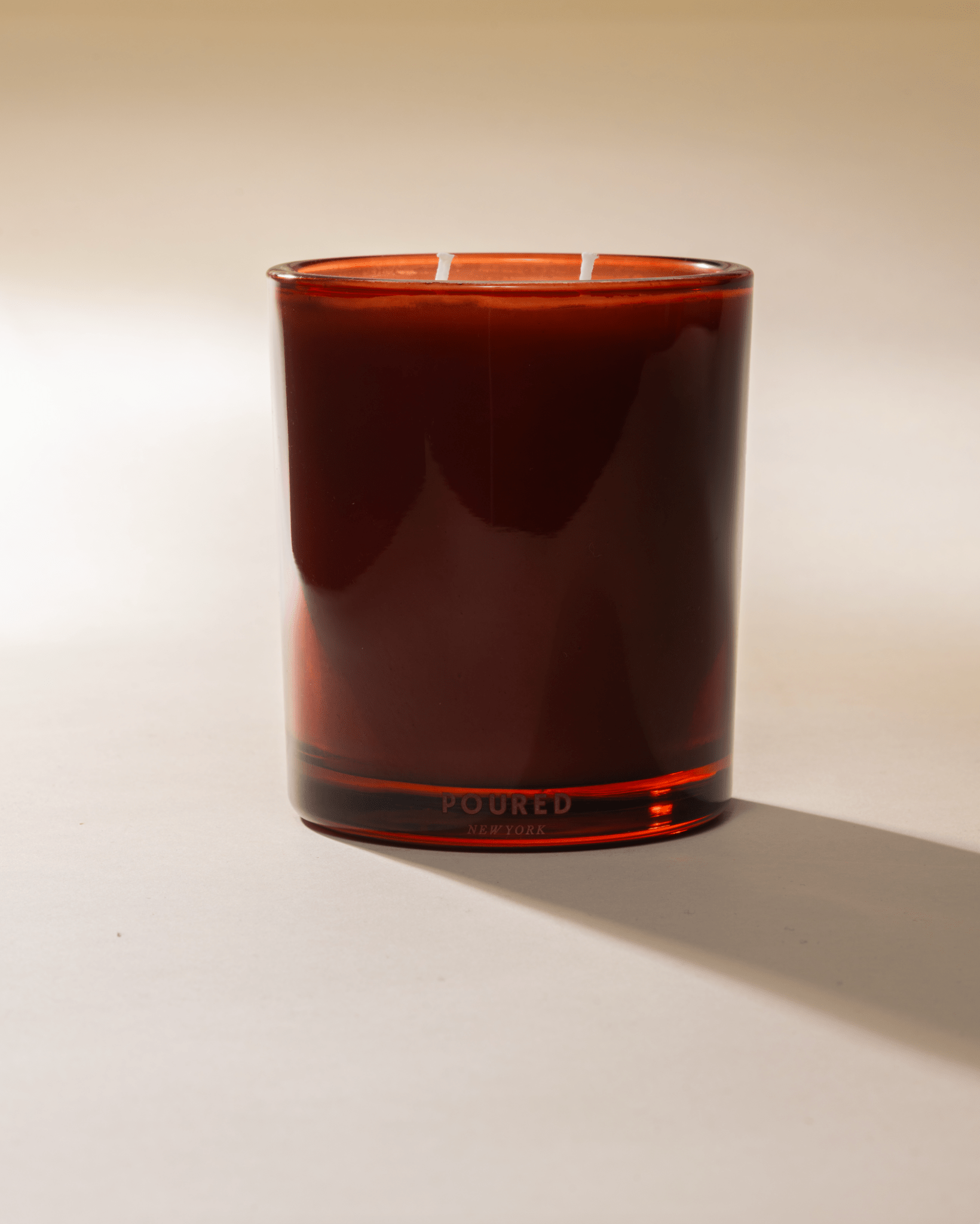 Poured New York 'Negroni Nights' two wick candle in red glass jar on a neutral background.