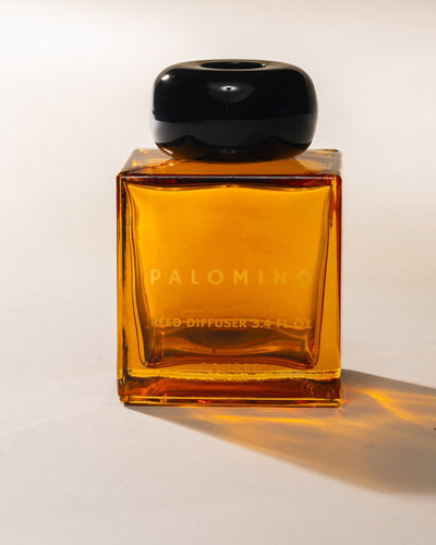 Amber glass 'Palomino' reed diffuser bottle with black cap on a white background